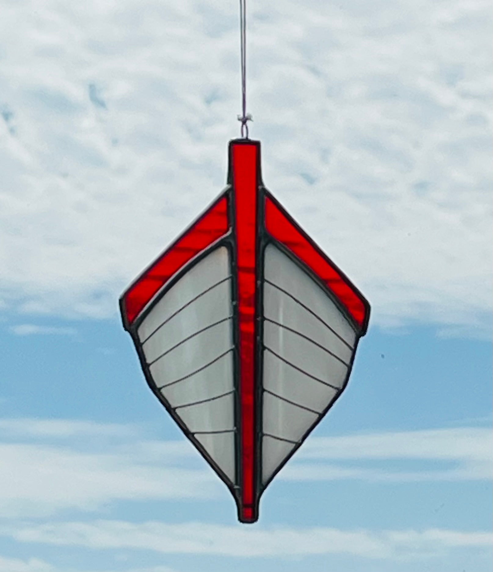 Our traditional punt-shaped stained glass suncatcher is white with a red trim. Hung with a blue sky background.
