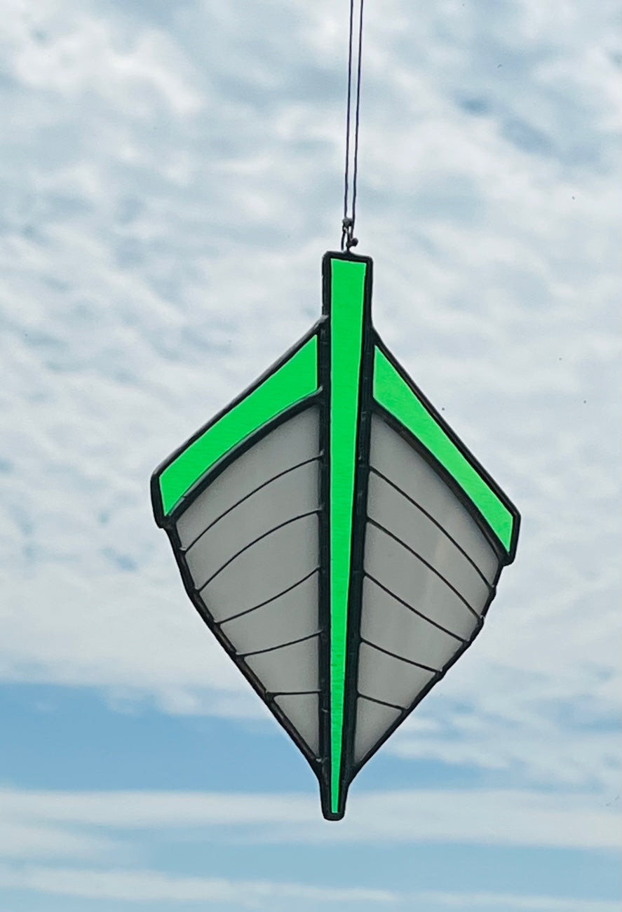 Our traditional punt-shaped stained glass suncatcher is white with a green trim. Hung with a blue sky background.