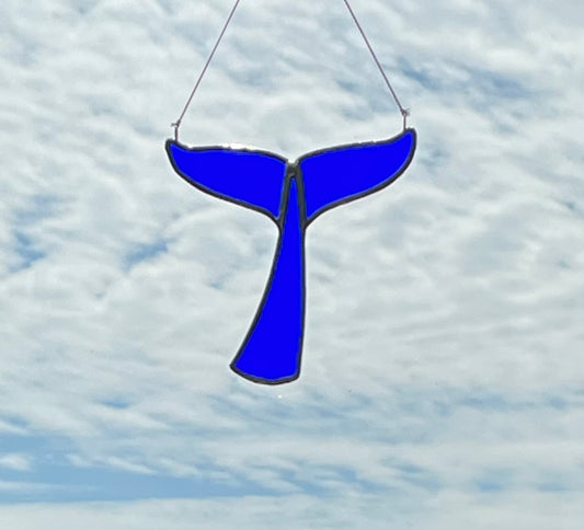 Dark blue whale tail suncatcher hung with a blue sky background.