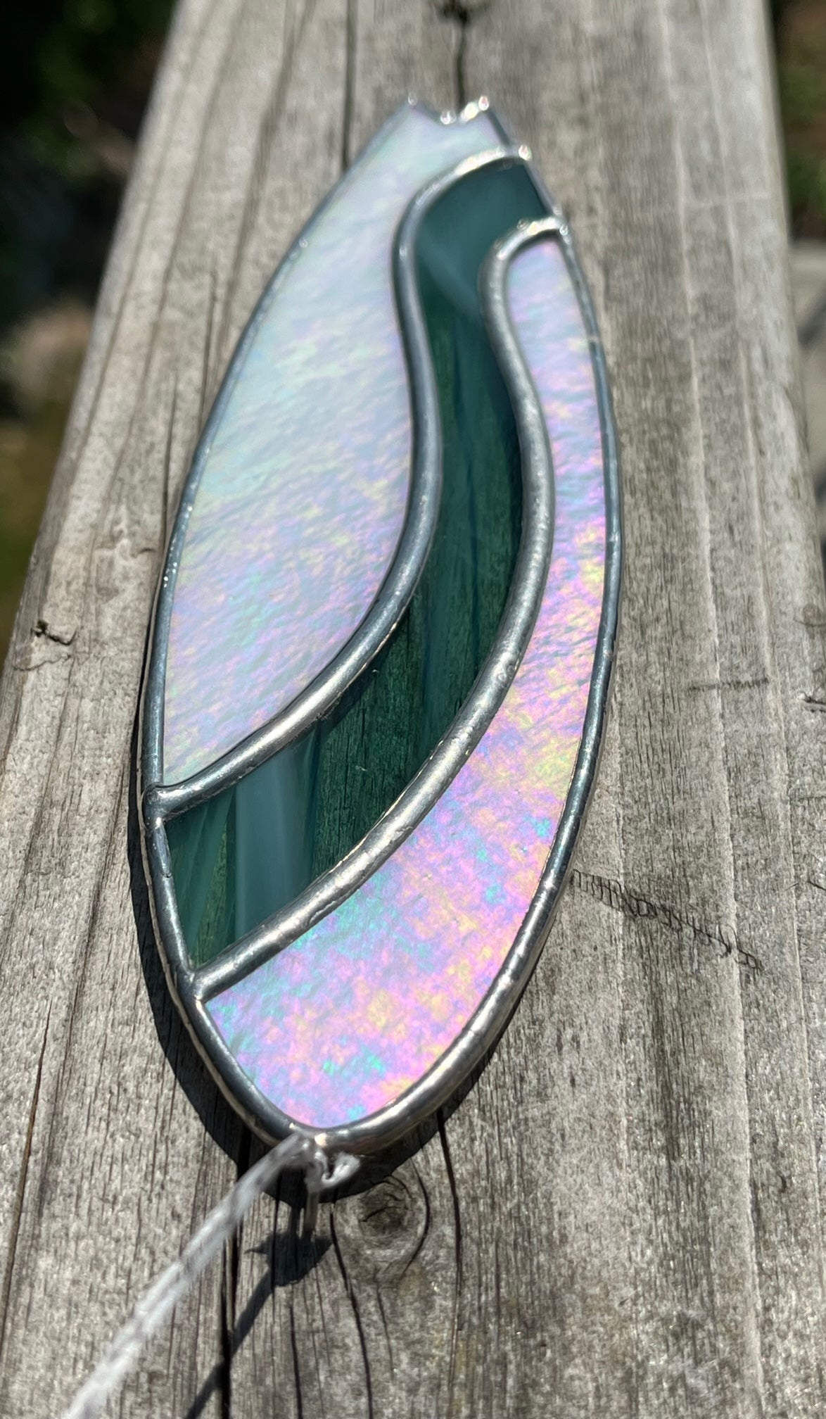 A stained glass shortboard that is made with white opalescent glass with a teal glass wave down the center. 