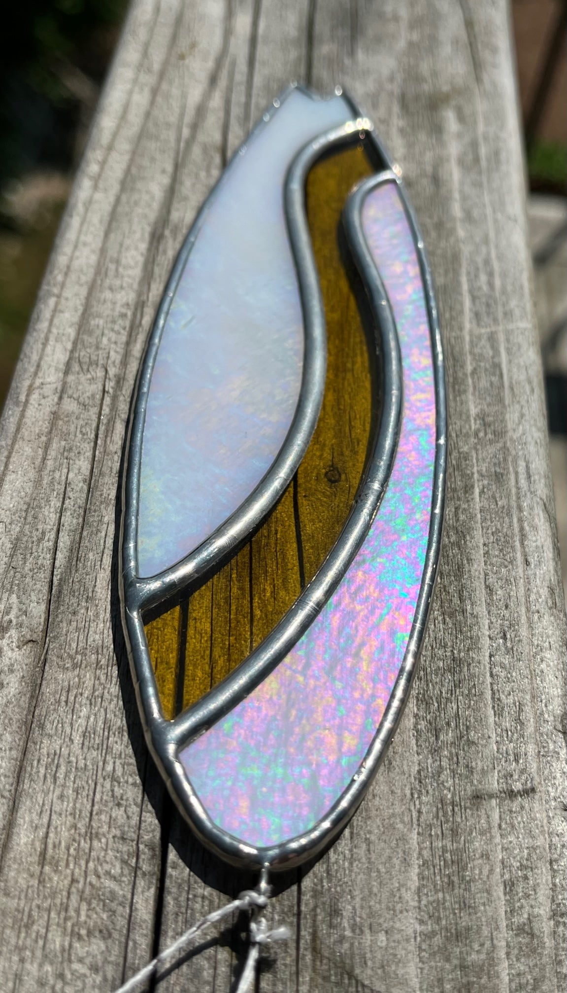 A stained glass shortboard that is made with white opalescent glass with a yellow glass wave down the center. 
