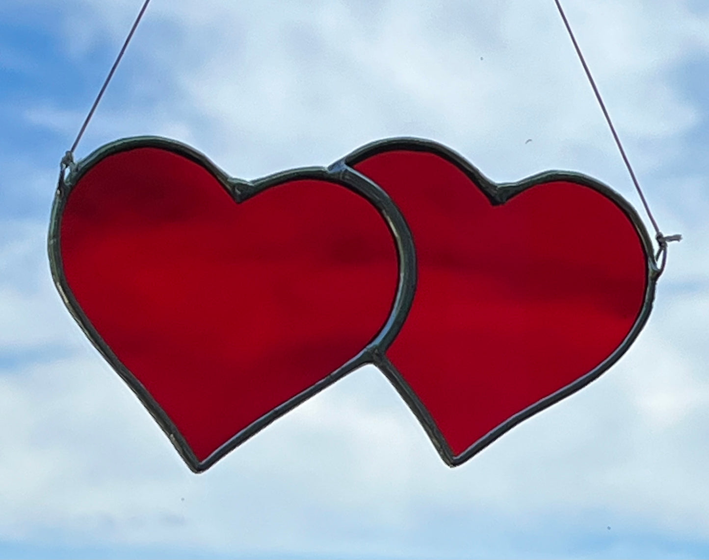 A suncatcher of red stained glass hearts joined together with a blue sky background.