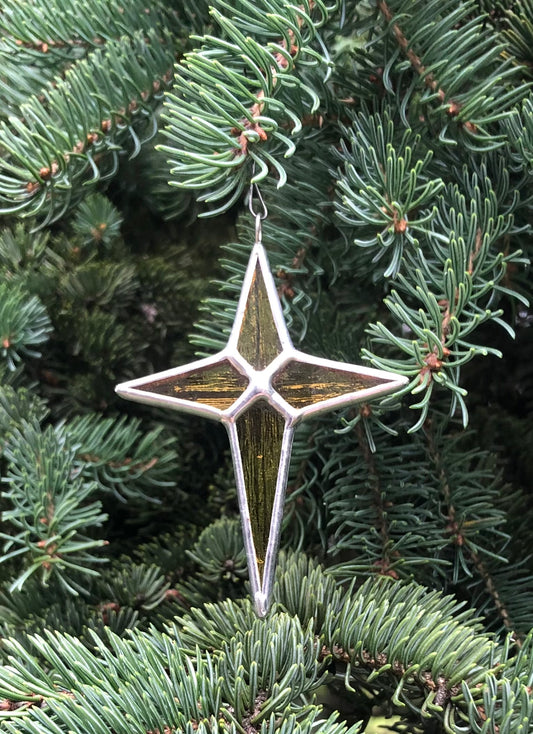 Stained glass Christmas star Christmas tree ornament made with  golden textured glass hanging on a spruce tree.