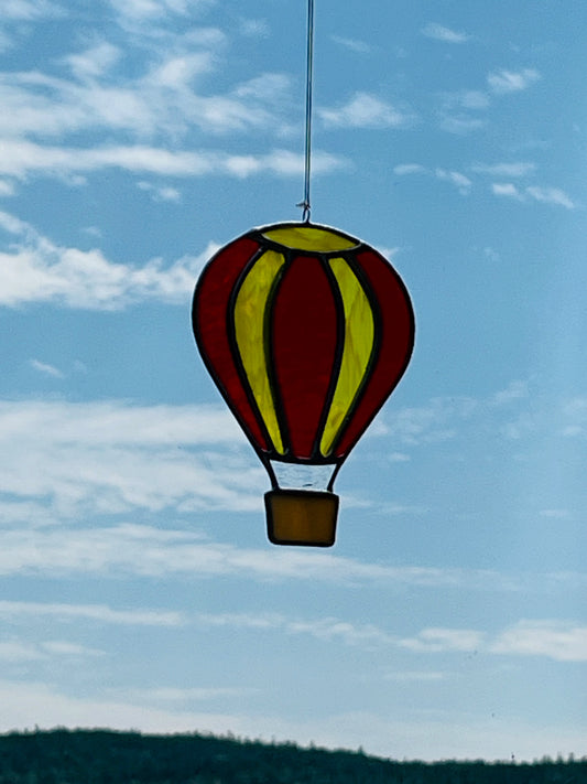 Red and yellow Stained glass hot air balloon with a tan basket hung with a blue sky background.